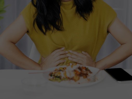 Woman sitting in front of a plate of food holding her stomach in discomfort