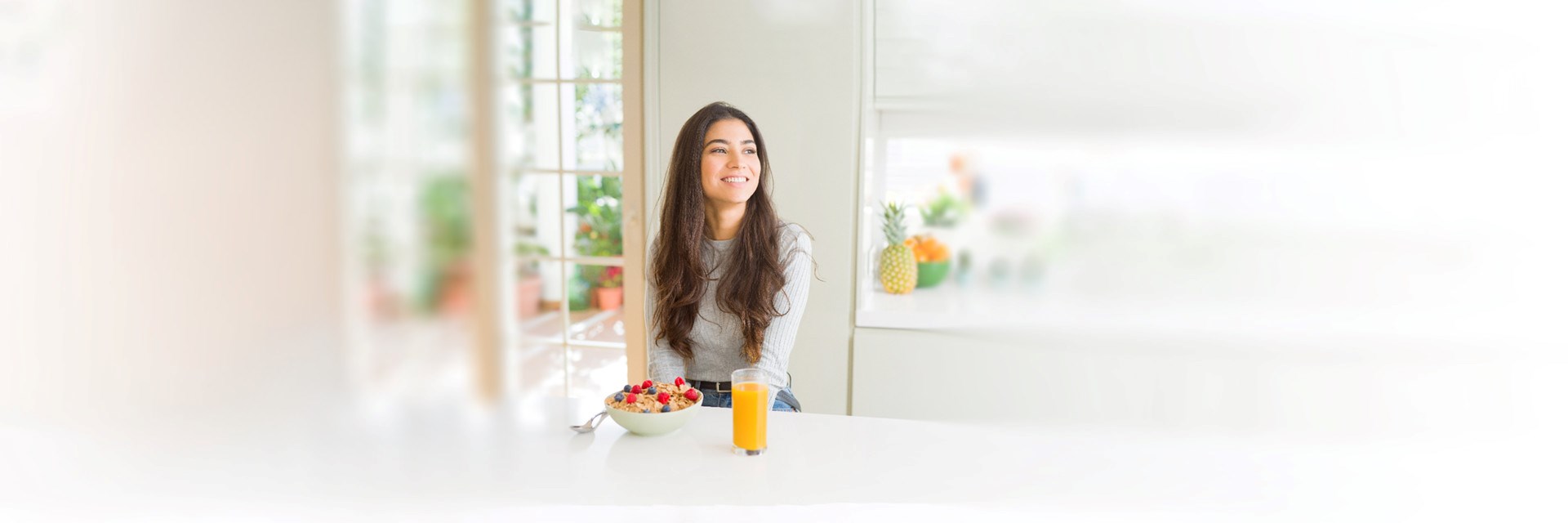 Young woman sat at kitchen counter with bowl of fruit and glass of orange juice