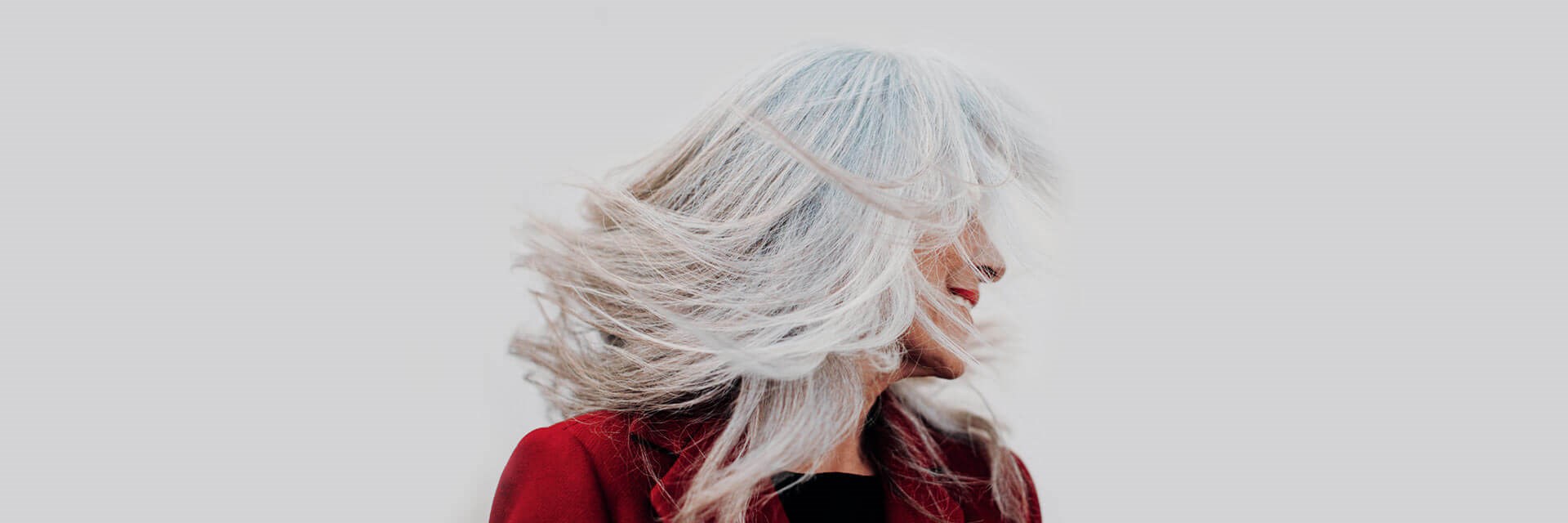 Grey-haired lady in red jacket tossing her hair