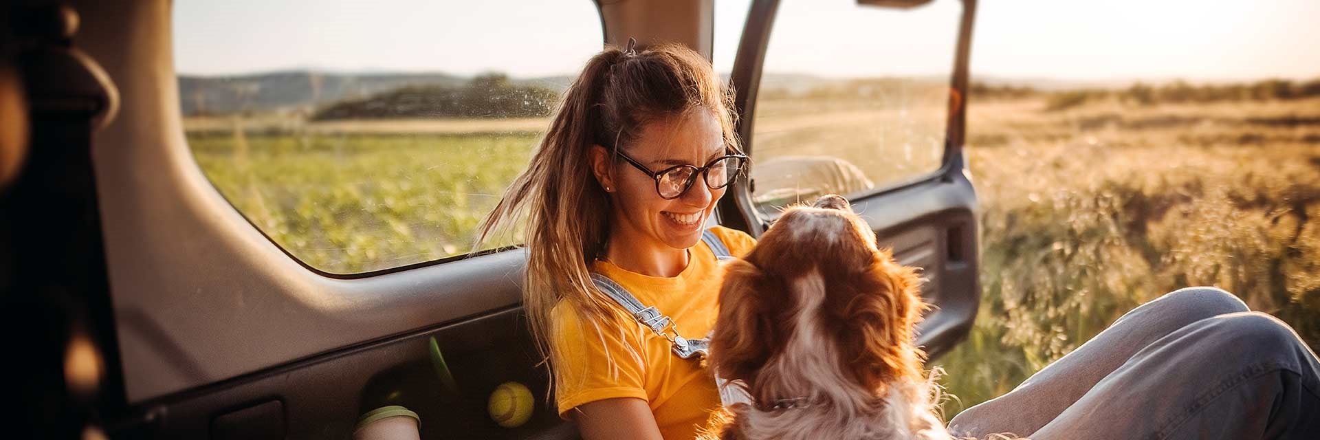 Woman and dog in a car with view of a sunny field behind