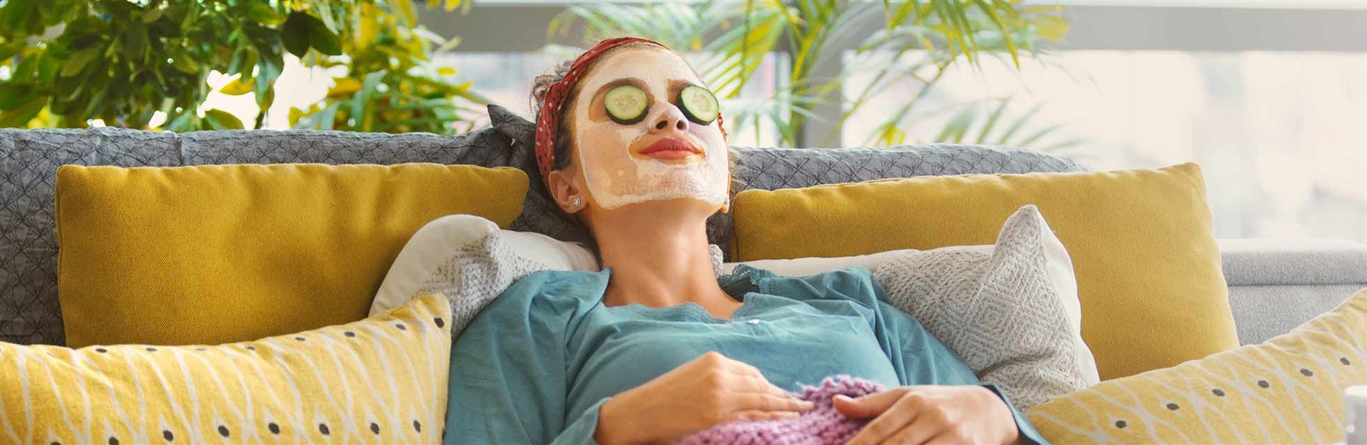 Woman lying on her sofa with a face mask on and cucumbers on her eyes