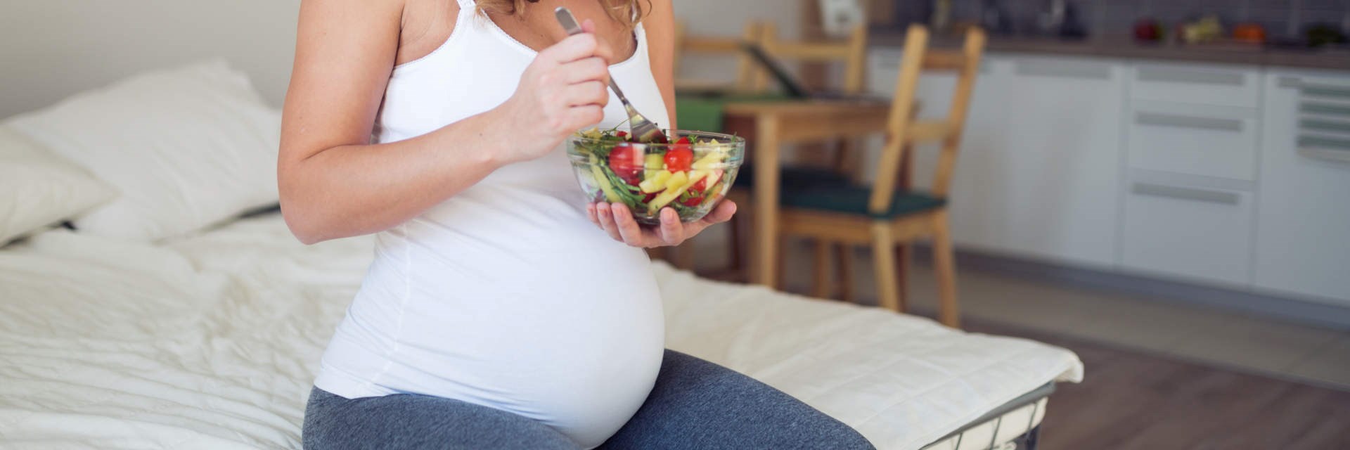 Photo of pregnant woman eating a salad on her bed