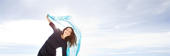 A woman smiling and dancing with a blue scarf in the sunshine