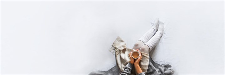 Overhead photo of woman holding cup of tea sitting on white sheet
