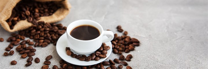 A cup of coffee surround by coffee beans
