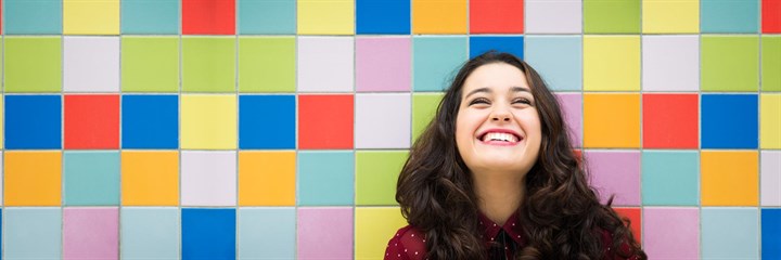 A woman smiling in front of a coloured background