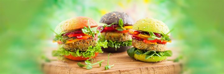 Three plant-based burgers on different coloured buns on a wooden plank with a green background