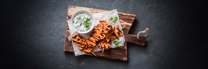 Chicken kebabs on wooden plate with tzatziki