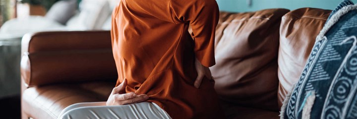 Woman on sofa holding back and stomach