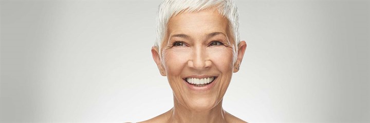 Mature woman with white hair smiling at the camera, on a grey background