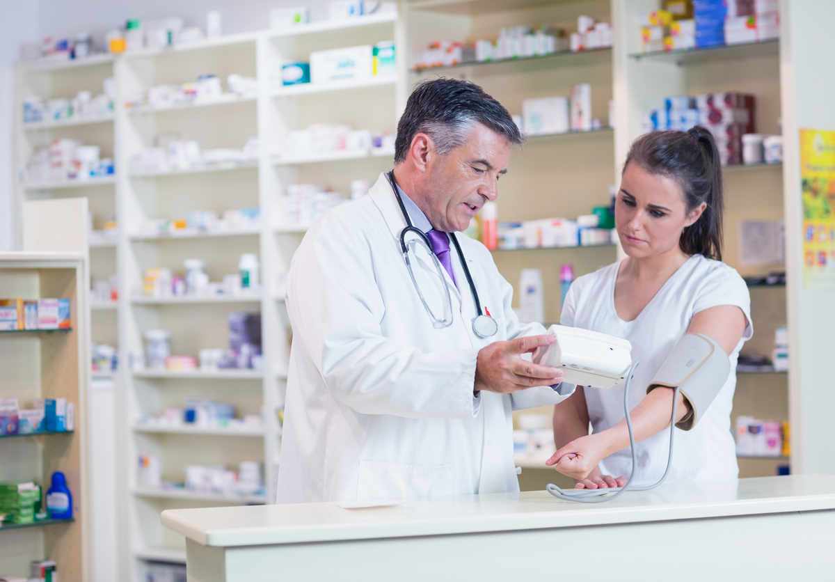 Male pharmacist checking young brunette woman's blood pressure in a pharmacy setting