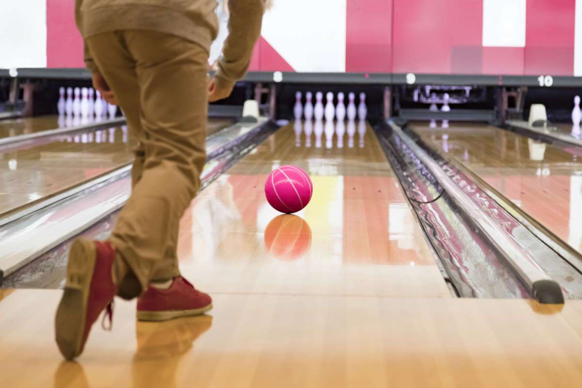 Shot from behind of man bowling red ball down alley