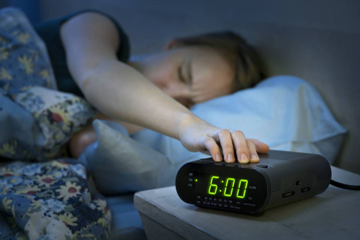 Woman turning off alarm clock set to 6am