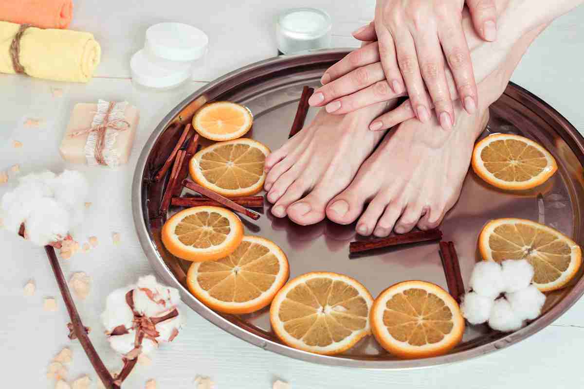 Woman's feet and hands on a tray with orange peel and flowers