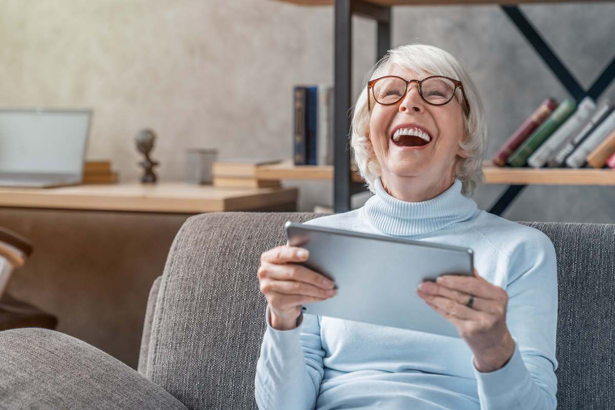 Older lady holding an iPad and laughing 