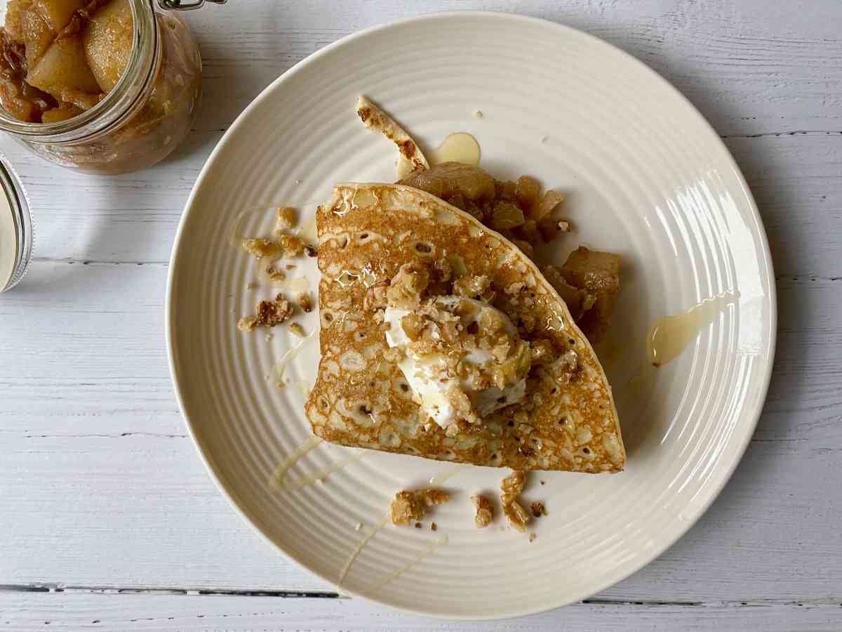 An overhead photo of a pancake filled with pear compote, topped with crème fraiche and chopped walnuts