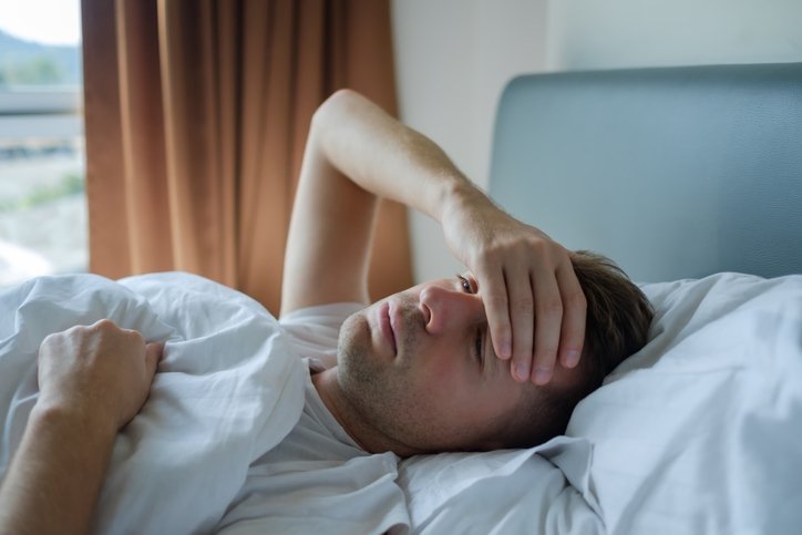 Man lying awake in bed with hand on head