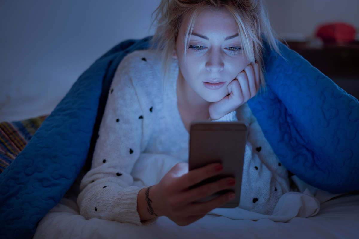 Woman looking at her phone under the bed covers
