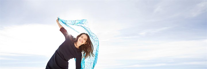 A woman smiling and dancing with a blue scarf in the sunshine