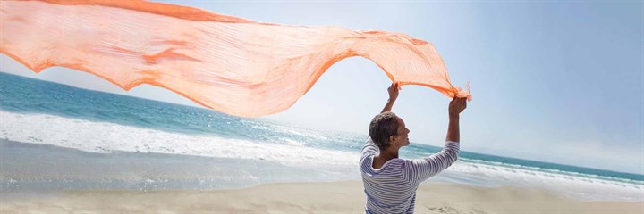 Image of a woman on a beach holding a orange material in the air
