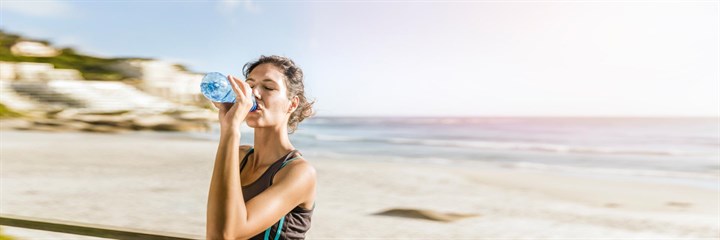 A woman drinking water and keeping hydrated after exercise on a beach