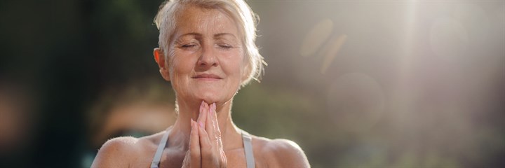 Mature woman with grey hair doing yoga outside looking peaceful