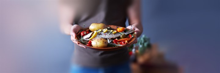 Person holding a plate of fish and vegetables
