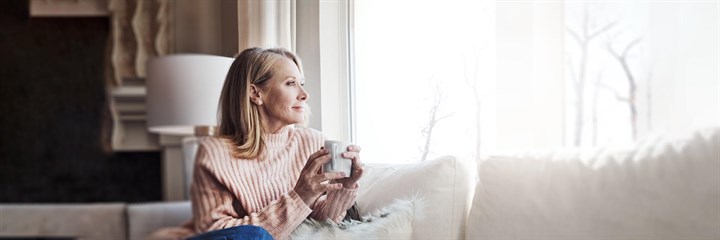 Woman on sofa with drink in hand looking out of the window